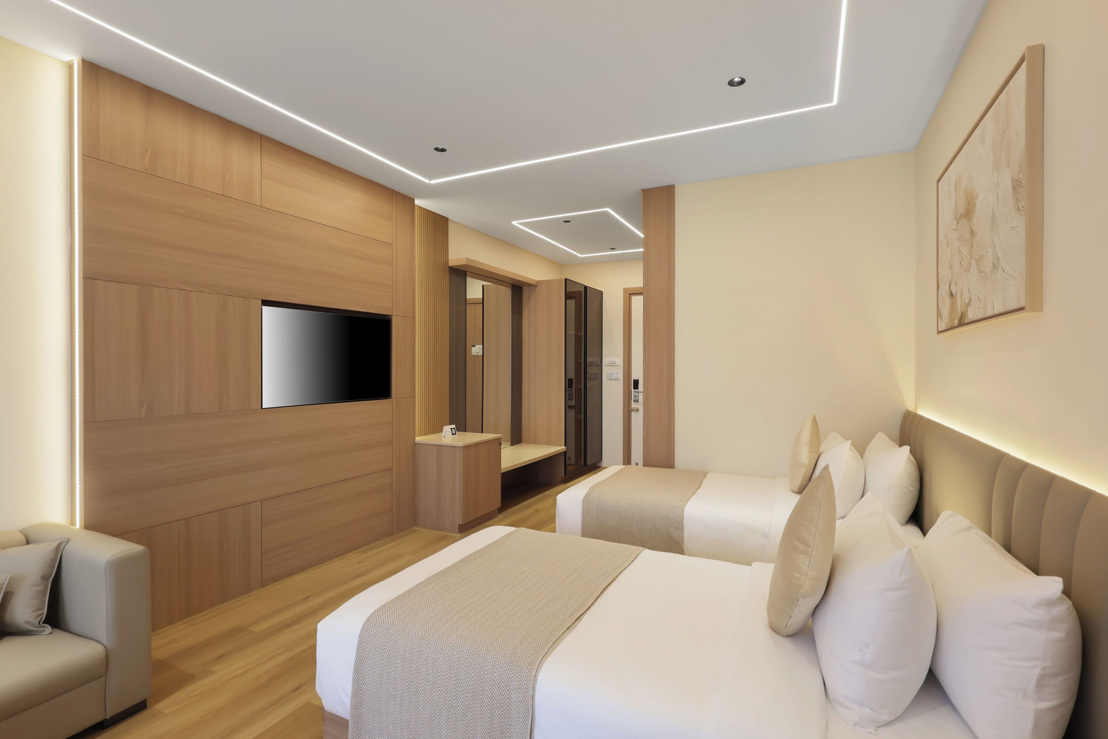 A modern hotel room with a flat-screen TV mounted on the wall, a sofa, two beds with white bedding, and a wooden panel wall.