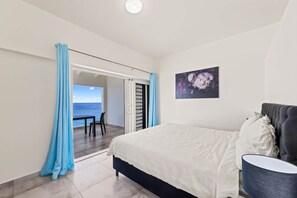 A bedroom with a bed, a nightstand, a painting, and a view of the sea through an open door. - LagunBay Oceanfront Breeze (Lagun)