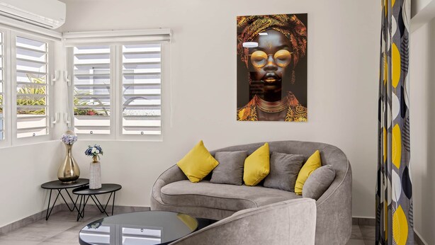 Una sala moderna con un sofá gris, cojines amarillos, una mesa de centro de cristal y un jarrón decorativo.