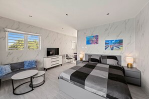 Ein modernes Schlafzimmer mit Bett, Fernseher, Sitzecke und Kunstwerken.