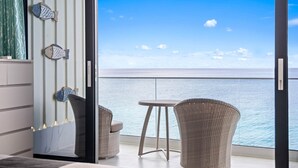 Ein Balkon mit Meerblick, zwei Korbstühle, ein kleiner Tisch und ein Bett mit grauem Kopfteil.