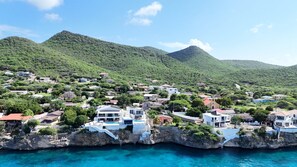 A coastal town with houses on a cliff overlooking the sea, a clear sky, and lush green hills in the background. - LagunBay Oceanfront Horizon (Lagun)