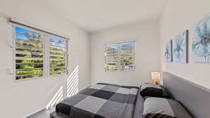 Un dormitorio con una cama, dos ventanas, una mesita de noche y decoración en la pared.