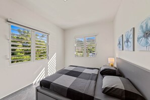 Ein Schlafzimmer mit einem Bett, zwei Fenstern, einem Nachttisch und Wandbildern.