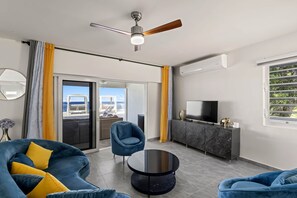 Ein modernes Wohnzimmer mit einer Couch, einem runden Couchtisch, einem Deckenventilator, einem Fernseher und einem Balkon mit Sitzgelegenheit.