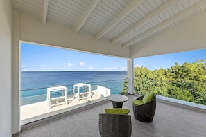 A balcony with a view of the ocean and a lush green landscape. - LagunBay Oceanfront Horizon (Lagun)
