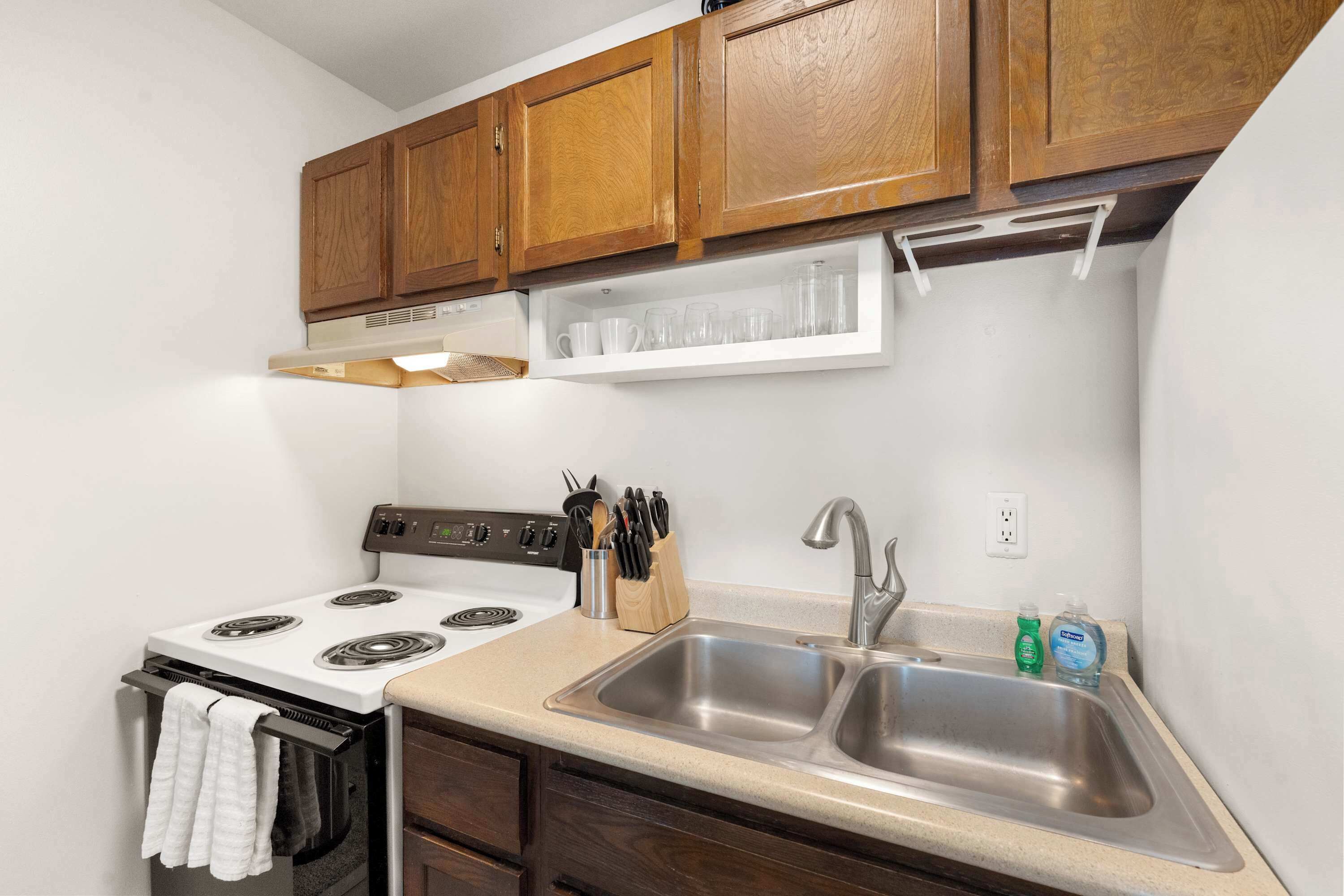 A compact kitchen with a stove, sink, and wooden cabinets.