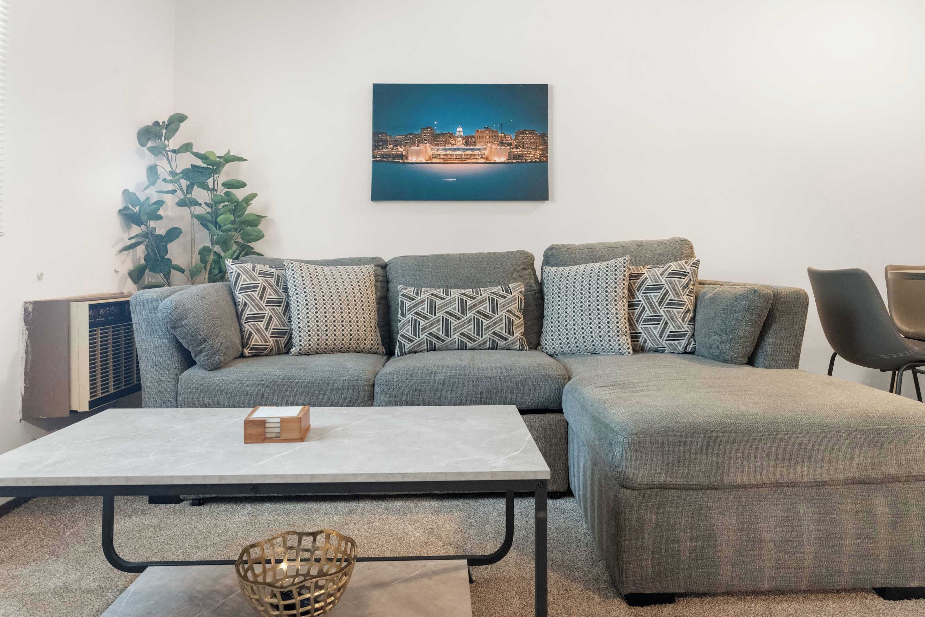 Ein Wohnzimmer mit einem Ecksofa, einem Couchtisch, einem Beistelltisch und einem gerahmten Bild an der Wand.