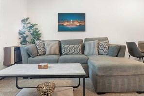 Ein Wohnzimmer mit einem Ecksofa, einem Couchtisch, einem Beistelltisch und einem gerahmten Bild an der Wand.