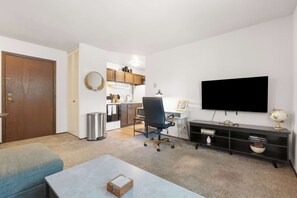 Ein kompakter Wohnraum mit Küchenzeile, Flachbildfernseher und Bücherregal.