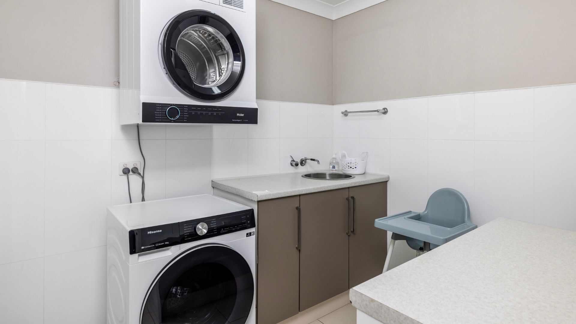 A compact laundry room with a front-loading washing machine, a sink, and a small chair.