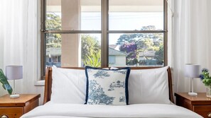 Un dormitorio con un ventanal grande, una cama con ropa de cama blanca y dos mesitas de noche con lámparas.