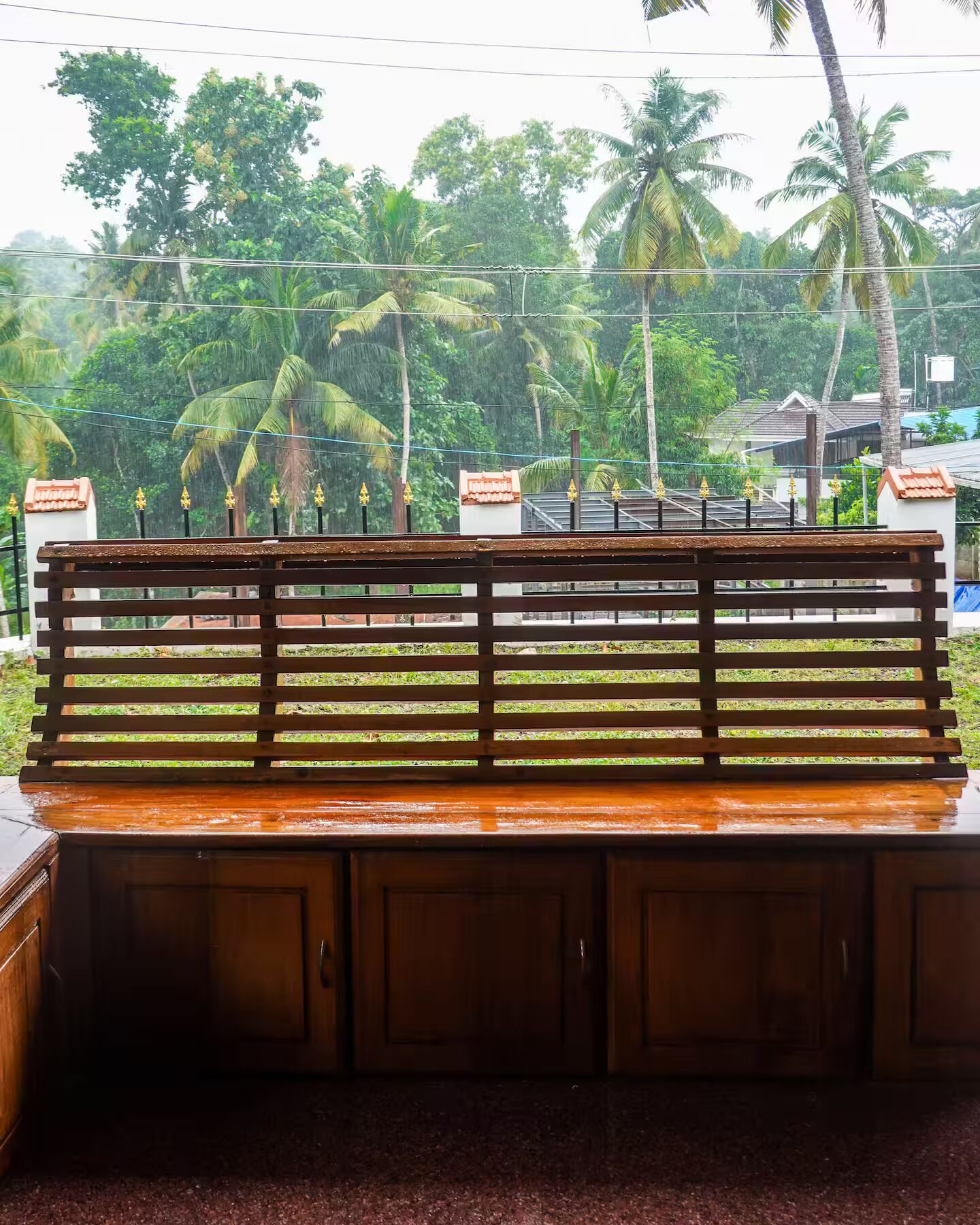 A wooden bench with a metal railing, set against a backdrop of lush greenery and a clear sky.
