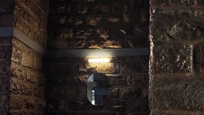 Un bagno con parete in pietra, uno specchio rotondo e mobili in legno.