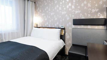 A hotel room with a bed, a desk, a chair, and a nightstand with a lamp.