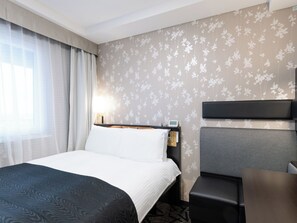 Una habitación de hotel con una cama, un escritorio, una silla y una mesita de noche con lámpara.