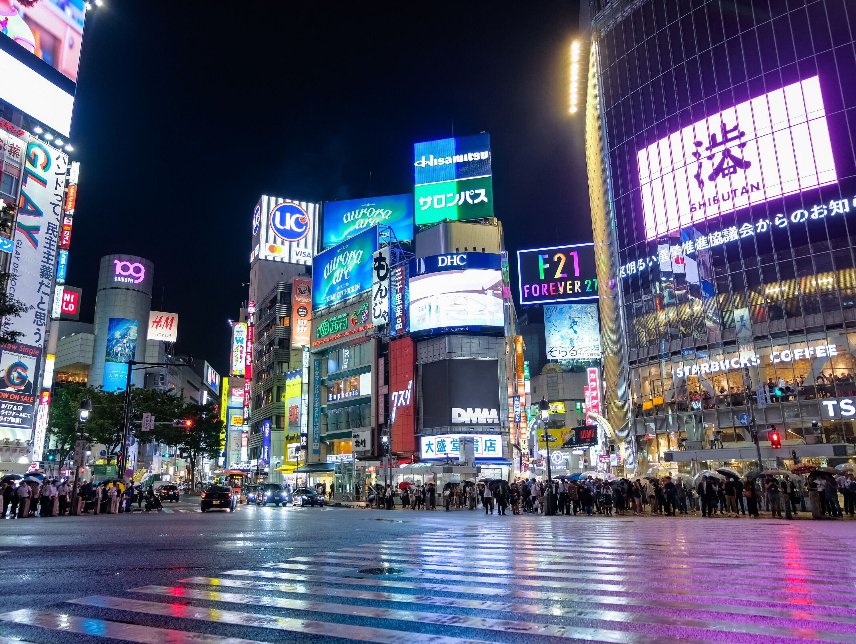 A busy urban street at night with illuminated billboards and storefronts.