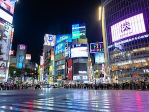 A busy urban street at night with illuminated billboards and storefronts.