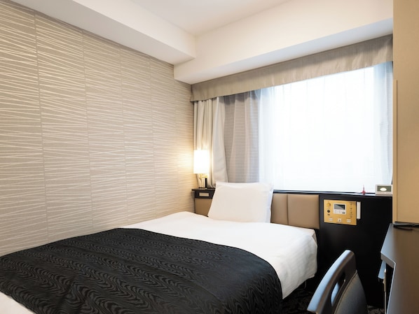 Una habitación de hotel con cama, mesita de noche, lámpara, ventana con cortinas y panel de control en la pared.