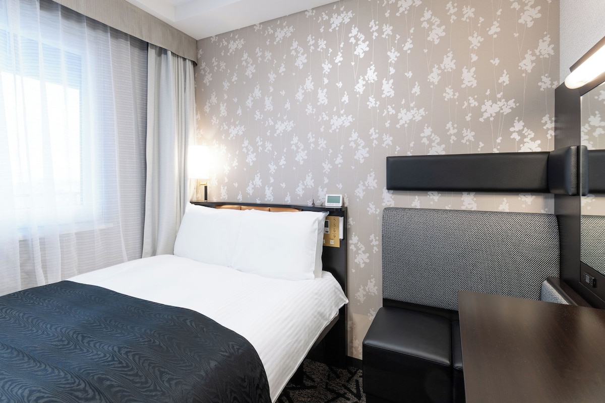Una habitación de hotel con una cama, un escritorio, una silla, una lámpara y un reloj de pared.