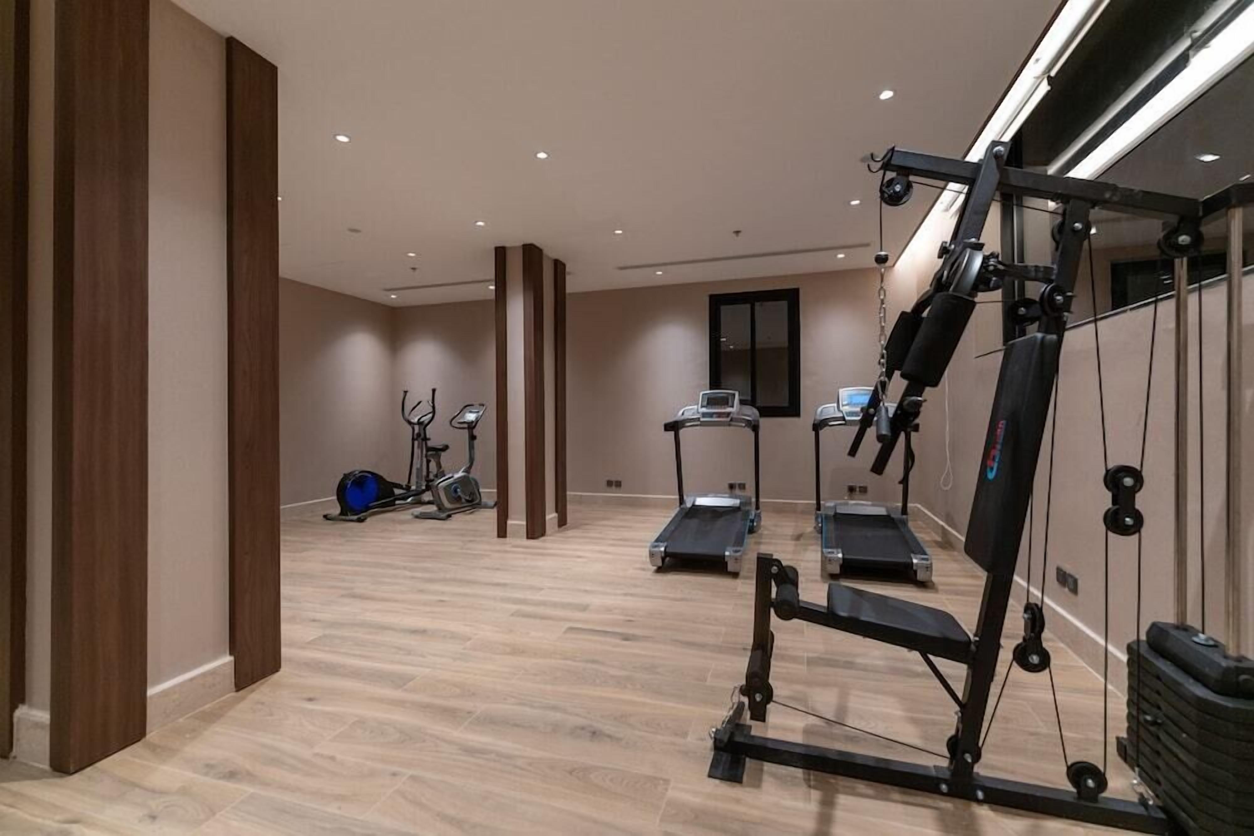 Un gimnasio con máquinas de cardio, equipo de levantamiento de pesas y un espejo grande.