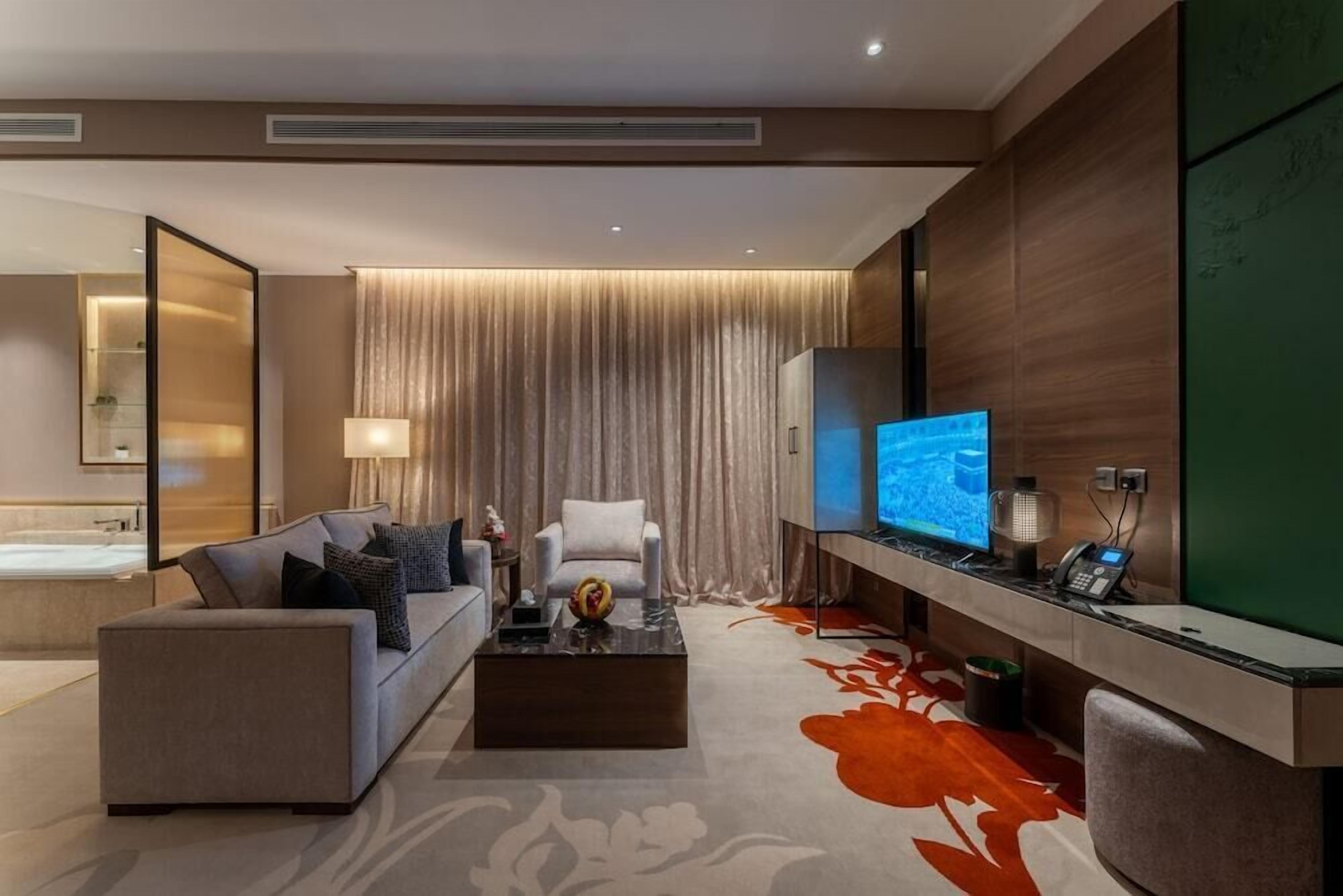 Una habitación de hotel moderna con sofá, sillón, televisor de pantalla plana y escritorio con teléfono.