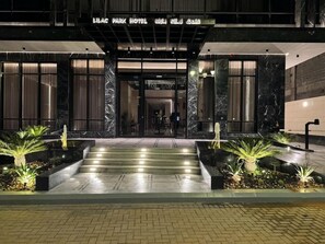 A hotel entrance with a marble facade, a staircase leading up to the entrance, and a well-lit pathway.