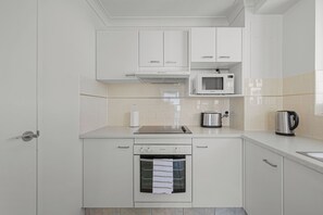Une cuisine moderne avec des meubles blancs, un four à micro-ondes encastré, une bouilloire et un lave-vaisselle.