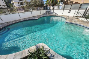 Une piscine aux eaux cristallines, à bords incurvés, entourée d’un petit muret et d’une clôture en métal.