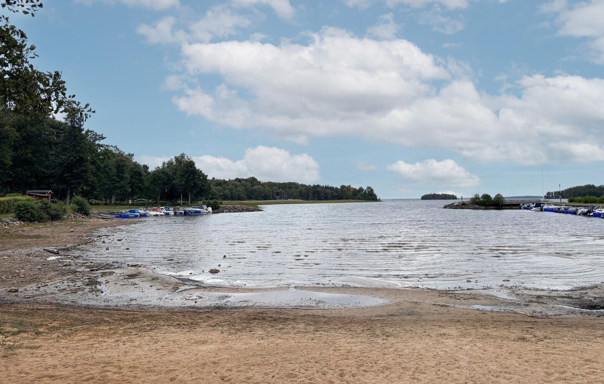 Uma praia com barcos atracados, uma faixa de areia e uma área arborizada ao fundo.