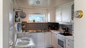 A kitchen with white cabinets, a stainless steel sink, a stove, and a window with a view of a blue roof. - 2 bedroom amazing home in Ljungby (Ljungby)