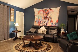 A living room with a dark blue wall, a black leather sofa, a round coffee table, and a large tapestry.