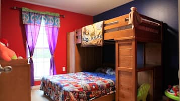 Un lit superposé avec une couverture aux couleurs vives, une fenêtre avec des rideaux violets et une petite chaise en forme de jouet.