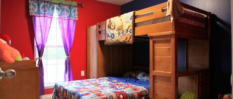 A bunk bed with a colorful quilt, a window with purple curtains, and a toy chair.