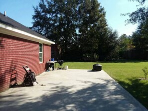 A backyard with a red brick house, a grill, and a barbecue table.