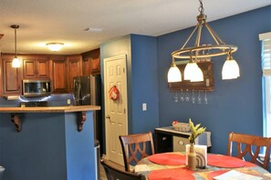 A kitchen with wooden cabinets, a microwave, and a refrigerator. There is a dining area with a table and chairs, and a chandelier above. - The "Home Over the Bridge" (Atmore)
