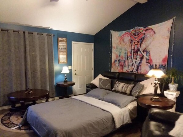 A bedroom with a bed, two bedside tables, a nightstand, a lamp, a curtain, and a tapestry on the wall.
