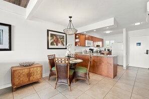 A modern kitchen with a dining area, featuring a central island, wooden cabinets, and a hanging light fixture.