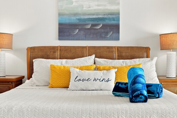 A neatly made bed with a white quilt, multiple pillows, and a rolled blue blanket.