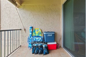 A balcony with a metal railing, a surfboard, a cooler, and several bags of diving gear.