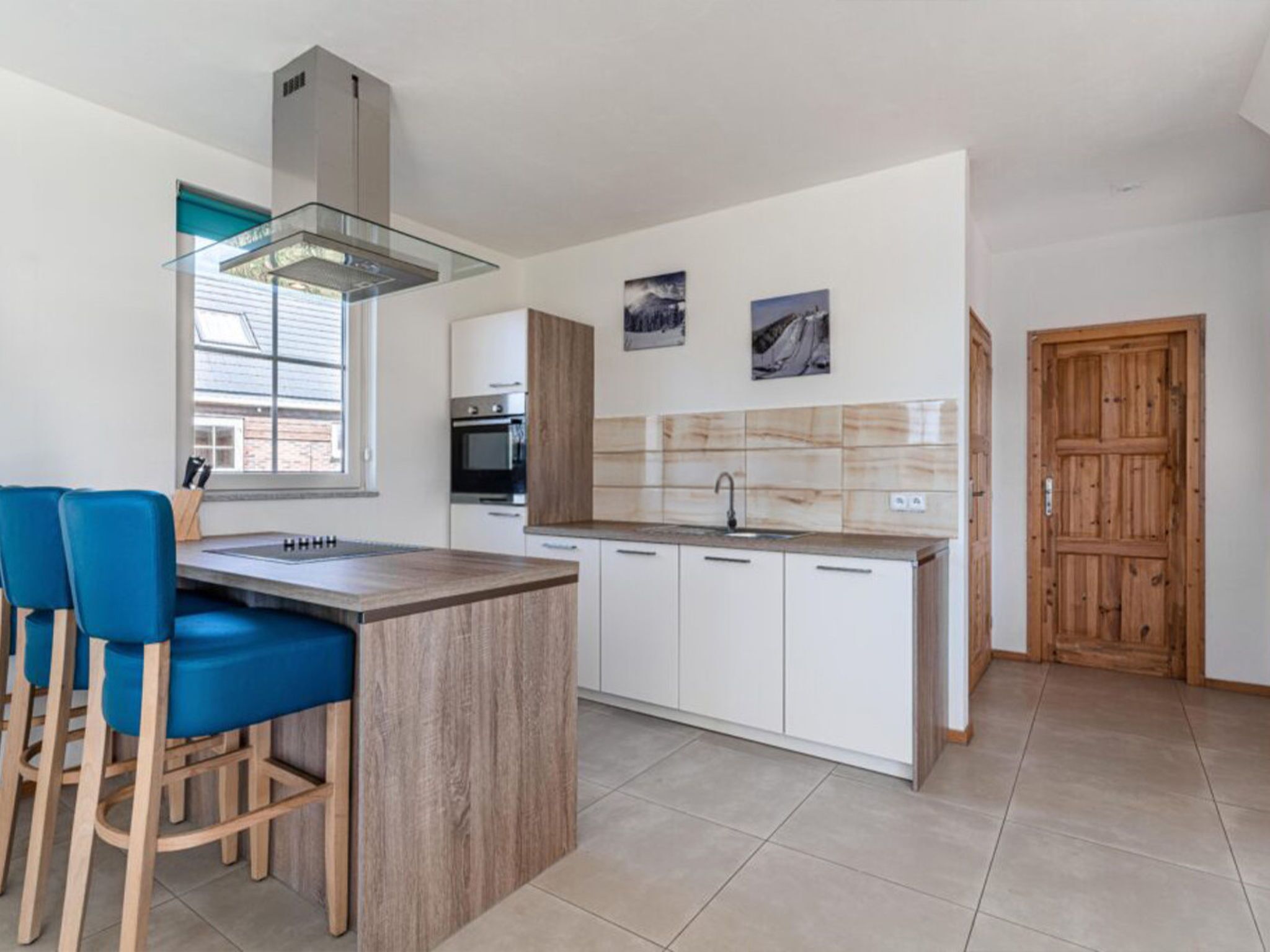 A modern kitchen with a central island, white cabinetry, and a wooden door.