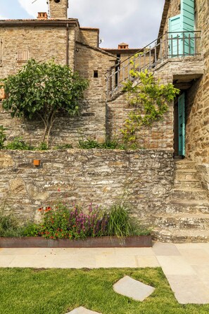 Un muro de piedra con un pequeño jardín, una reja de metal y un edificio con balcón.