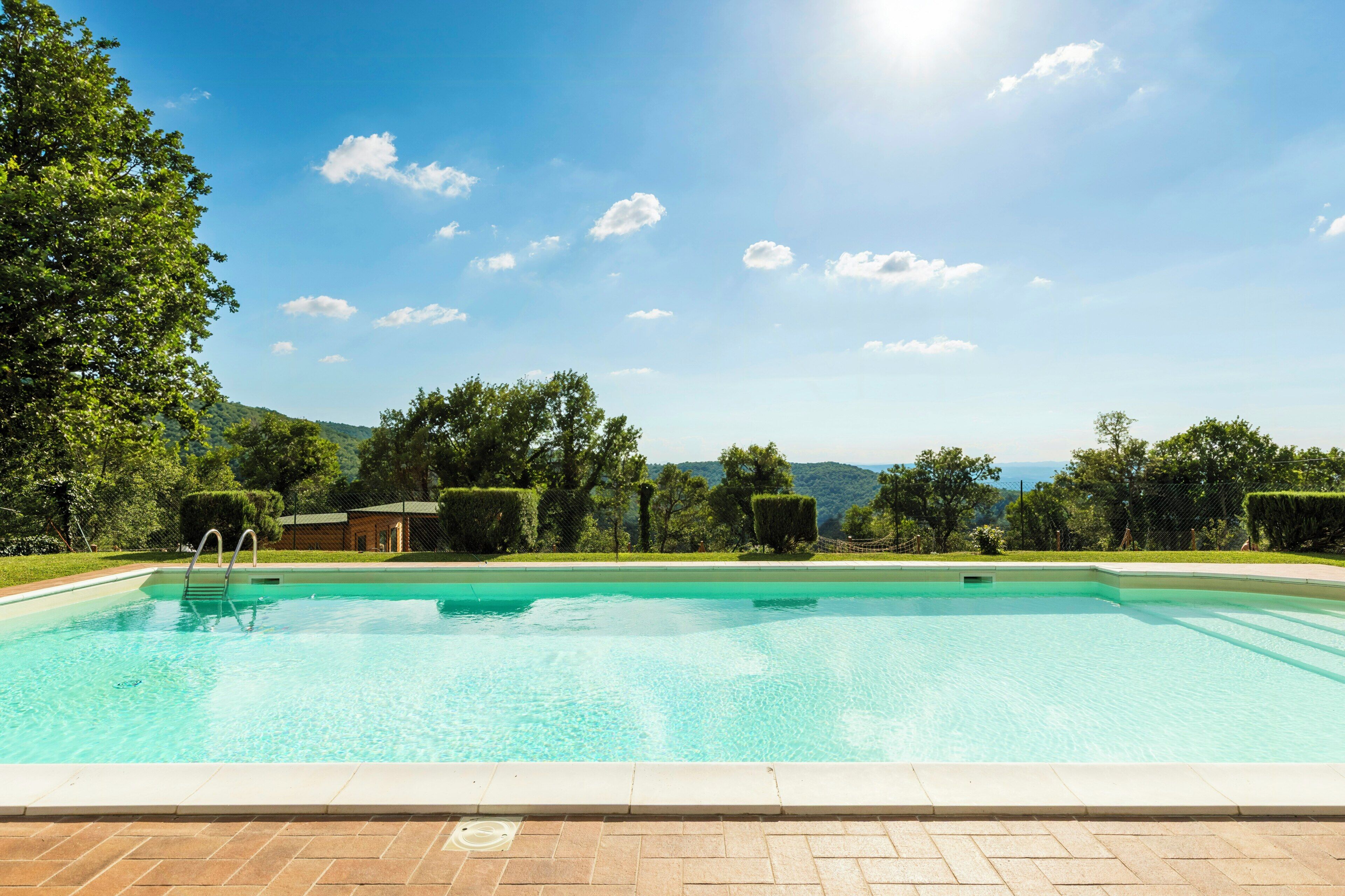 Una piscina rectangular con superficie de agua azul cristalina, rodeada por una solana pavimentada.