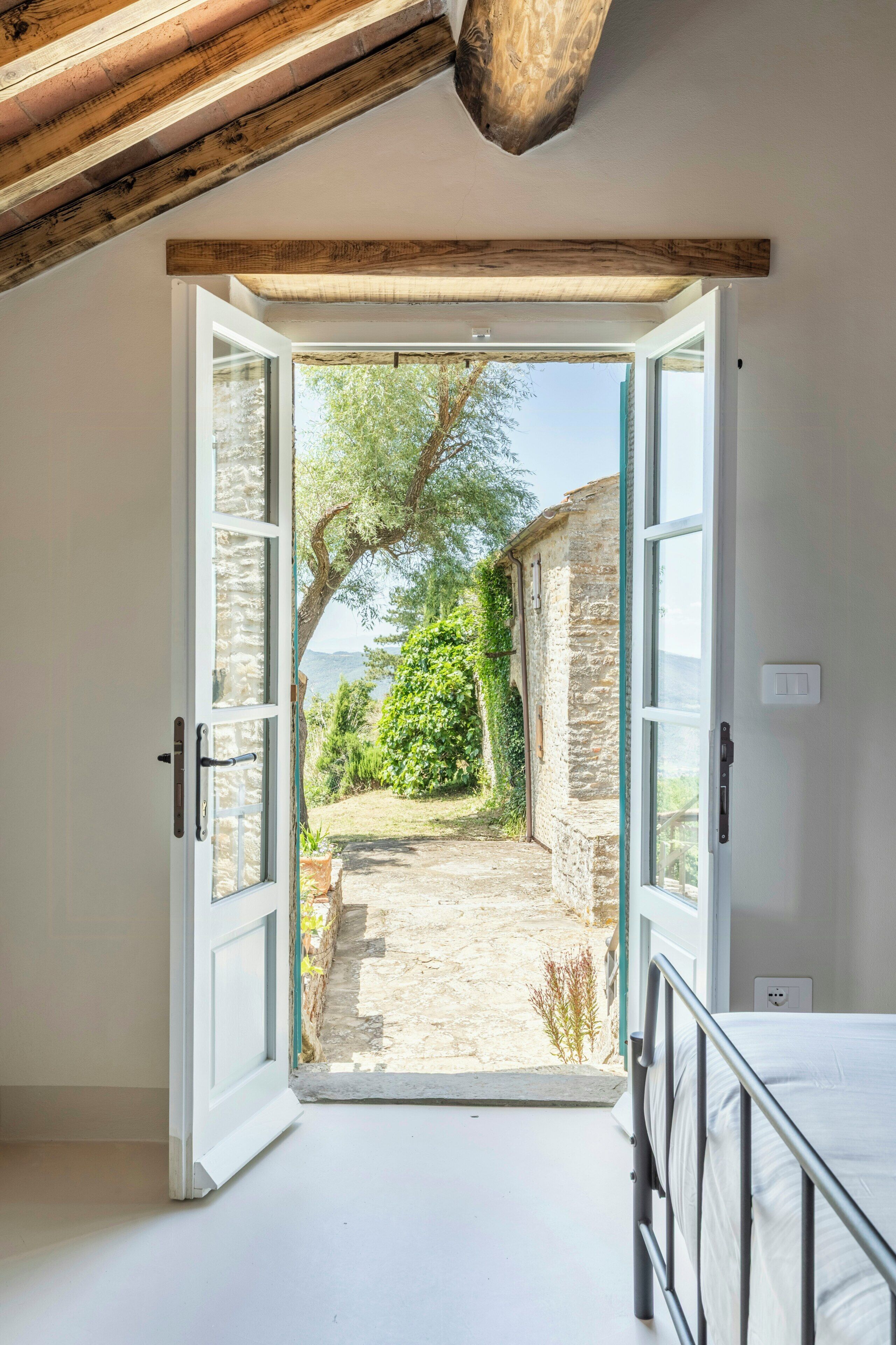 Une porte ouverte donne sur un chemin de pierre bordé de verdure et offre une vue sur le paysage.
