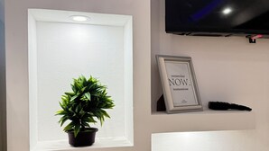 Pared com três luminárias embutidas, um vaso de planta, uma moldura com uma frase e um controle remoto.