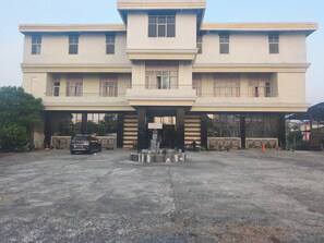 A hotel with a central entrance, multiple balconies, and a parking area.