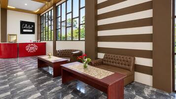 Un hall de hotel con una recepción, una zona de estar con un sofá y una mesa, y un amplio ventanal con vistas al exterior.