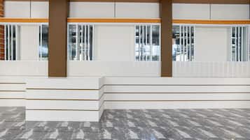 A spacious interior with a marble floor, white benches, and large windows with vertical blinds.