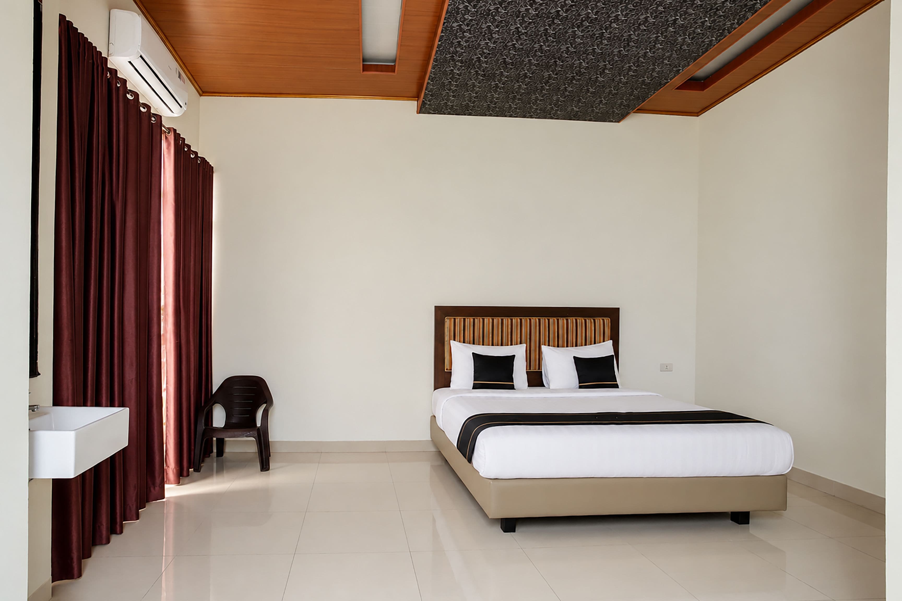 Una habitación de hotel con cama, una silla, un lavamanos y una ventana con cortinas.