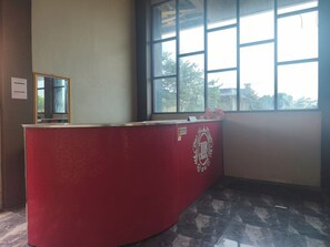 A hotel reception desk with a red finish, a large window with a view of trees, and a sign indicating a no-smoking area.